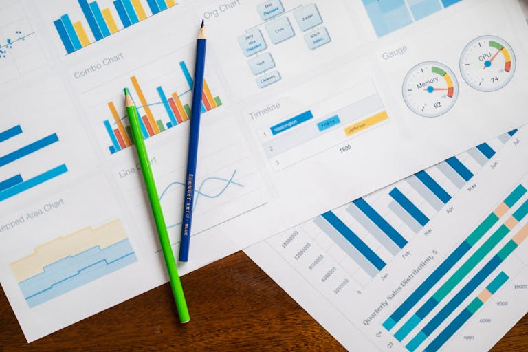 Flat lay of various business charts and colored pencils on wooden table, highlighting financial analysis.