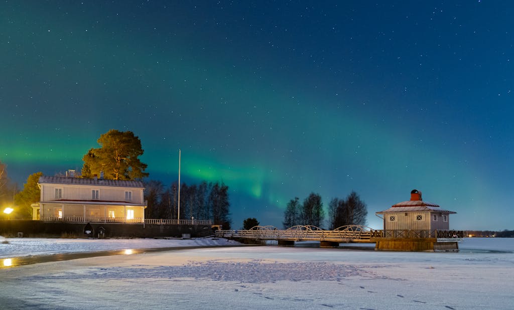 Stunning view of the Northern Lights shining over a frozen pier and building in Kokkola, Finland.